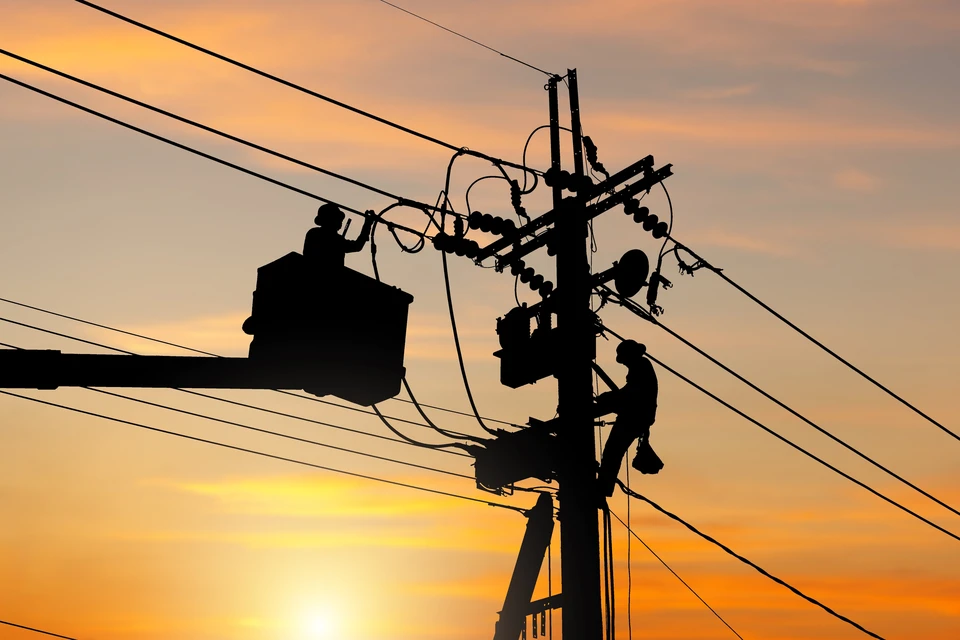 Sc&egrave;ne ext&eacute;rieure au coucher du soleil avec technicien en silhouette travaillant sur poteau &eacute;lectrique