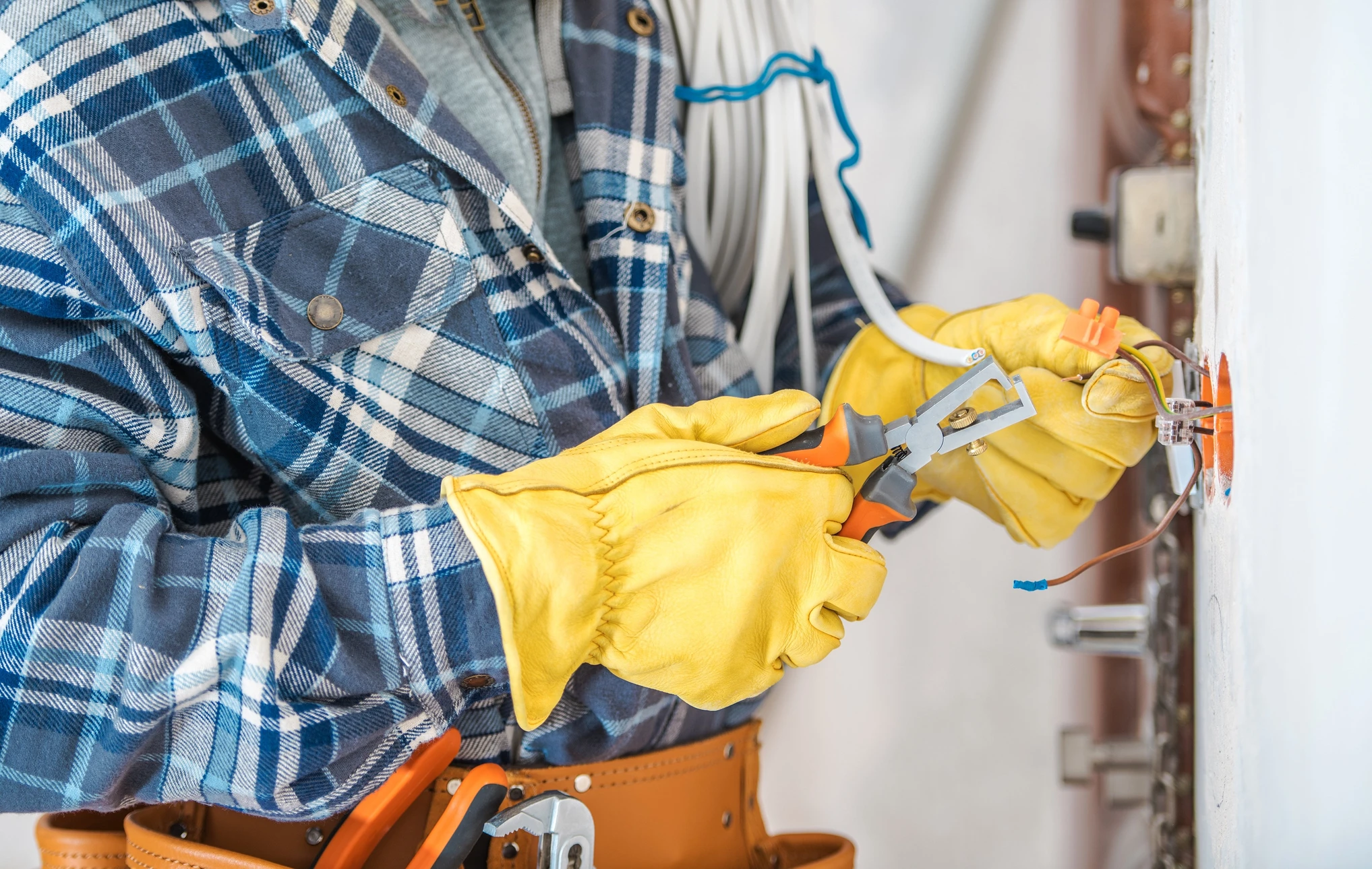 &Eacute;lectricien professionnel en chemise &agrave; carreaux travaillant sur installation &eacute;lectrique r&eacute;sidentielle, manipulant fils et connexions dans bo&icirc;tier mural blanc