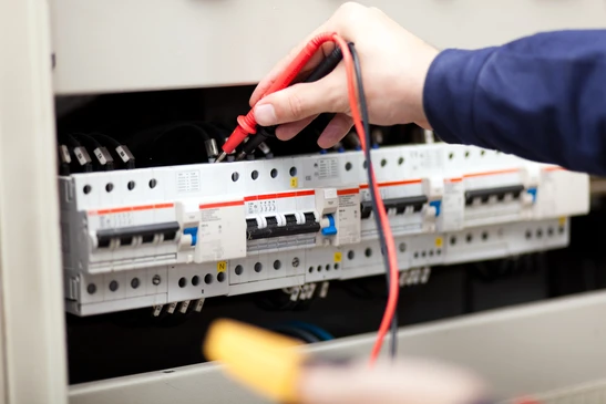 Int&eacute;rieur professionnel, technicien en veste bleue effectuant mesures &eacute;lectriques sur tableau de distribution
