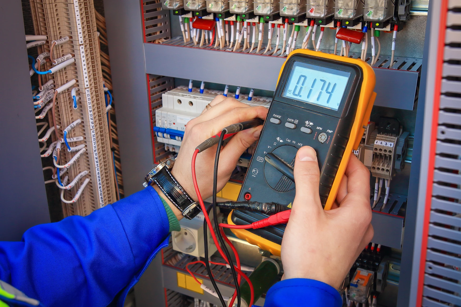 Technicien en vêtement de travail bleu effectuant des mesures électriques dans une armoire de distribution