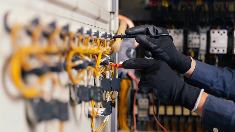 Technicien en combinaison bleue avec gants de protection noirs effectuant une intervention de maintenance sur équipement électrique industriel