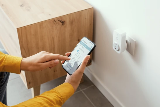 Femme mettant en place une prise intelligente &agrave; la maison en utilisant son smartphone, sa maison intelligente et son concept de domotique