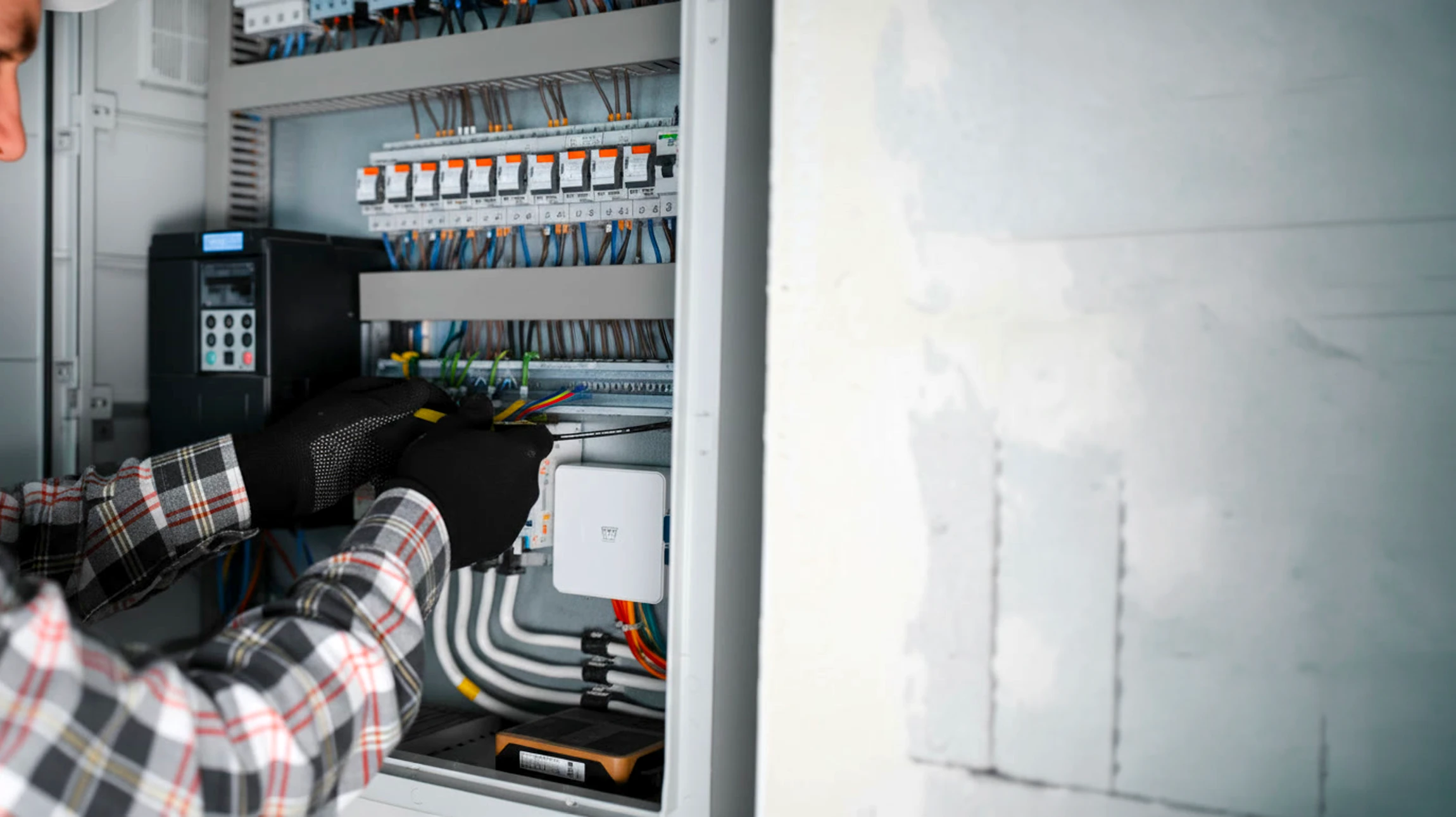 Technicien en chemise bleue travaillant sur armoire électrique industrielle, manipulant composants électroniques