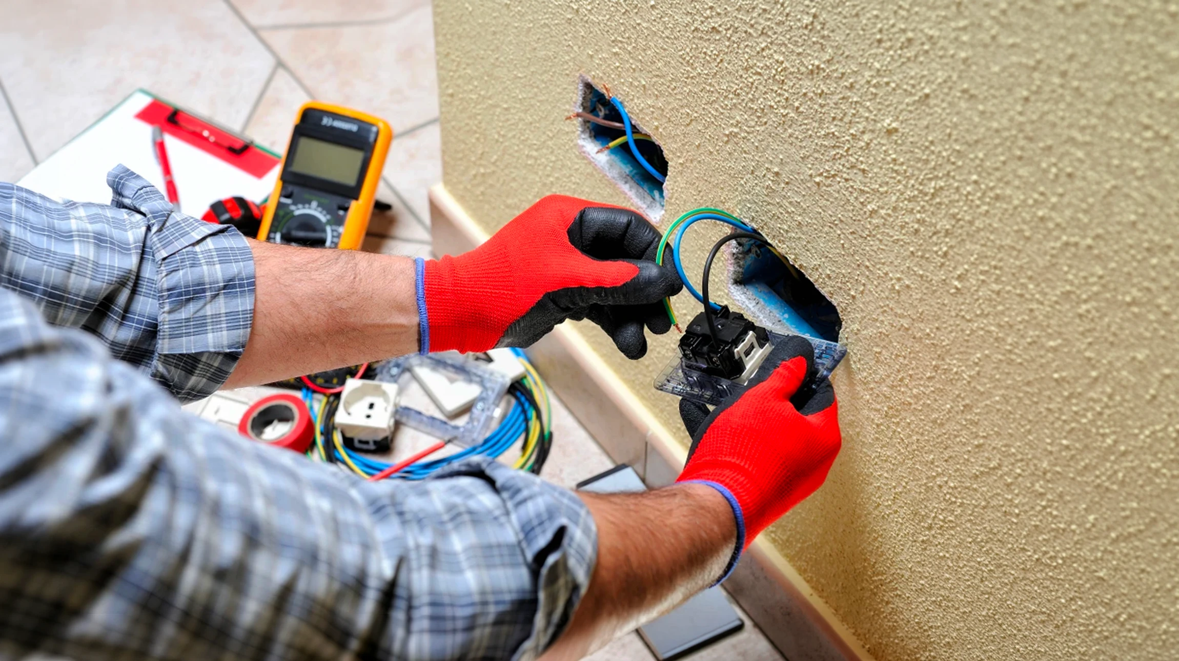 Électricien professionnel travaillant sur installation électrique résidentielle, manipulant multimètre et câblage dans boîtier mural