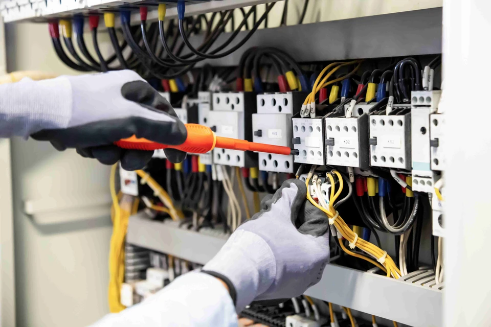 Électricien professionnel en tenue de travail avec gants blancs intervenant sur un tableau électrique industriel