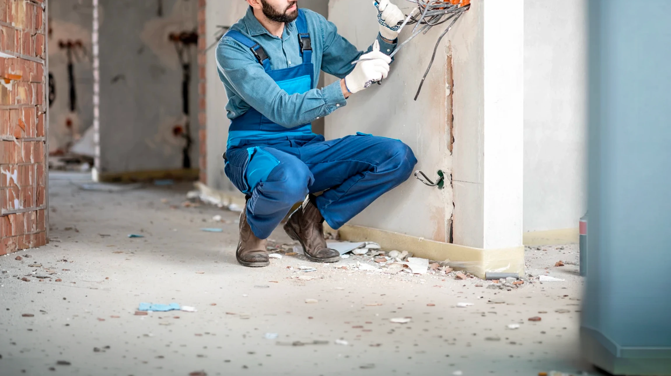 Électricien professionnel en salopette bleue et casquette travaillant dans un bâtiment en construction