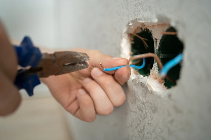 Électricien professionnel en gilet haute visibilité orange installant des câbles électriques dans une maison en construction